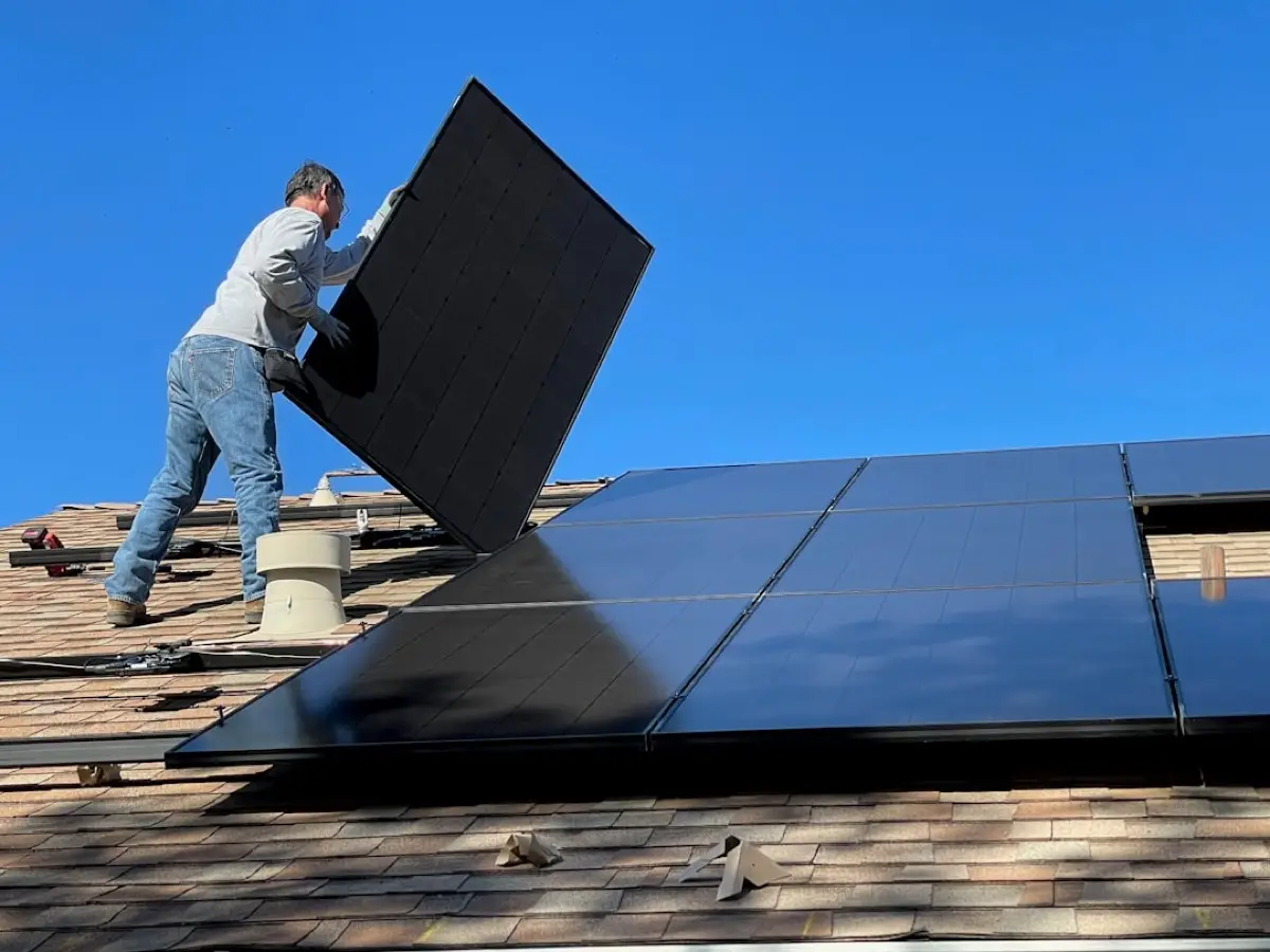 Montážník nese fotovoltaický panel po střeše rodinného domu